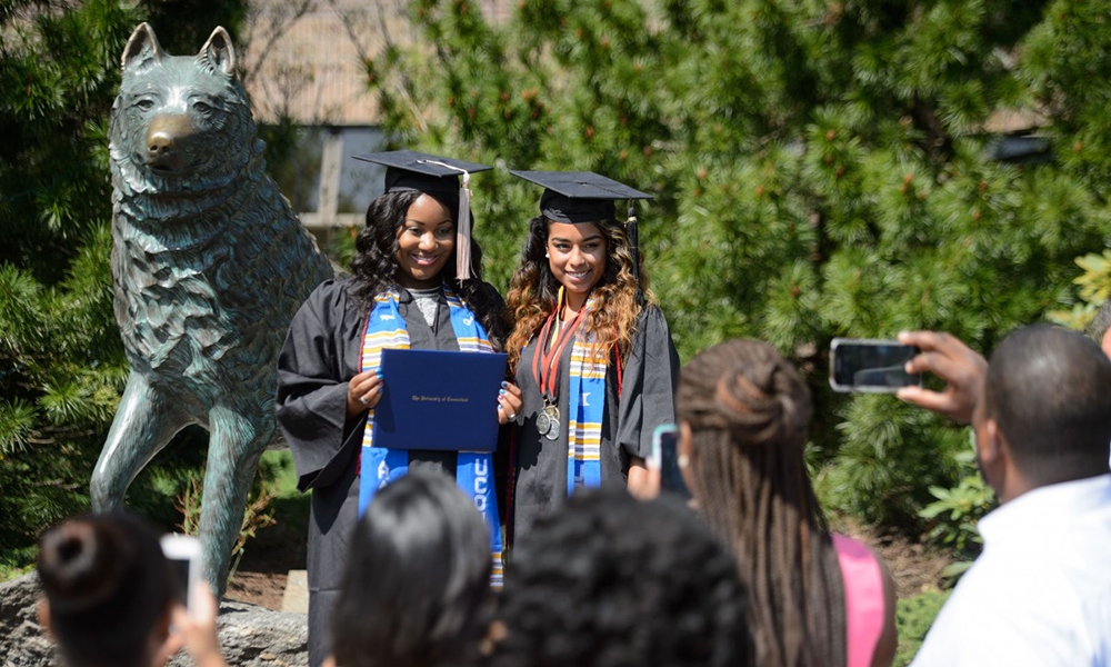 UConn graduates posing with Jonathan Husky statue